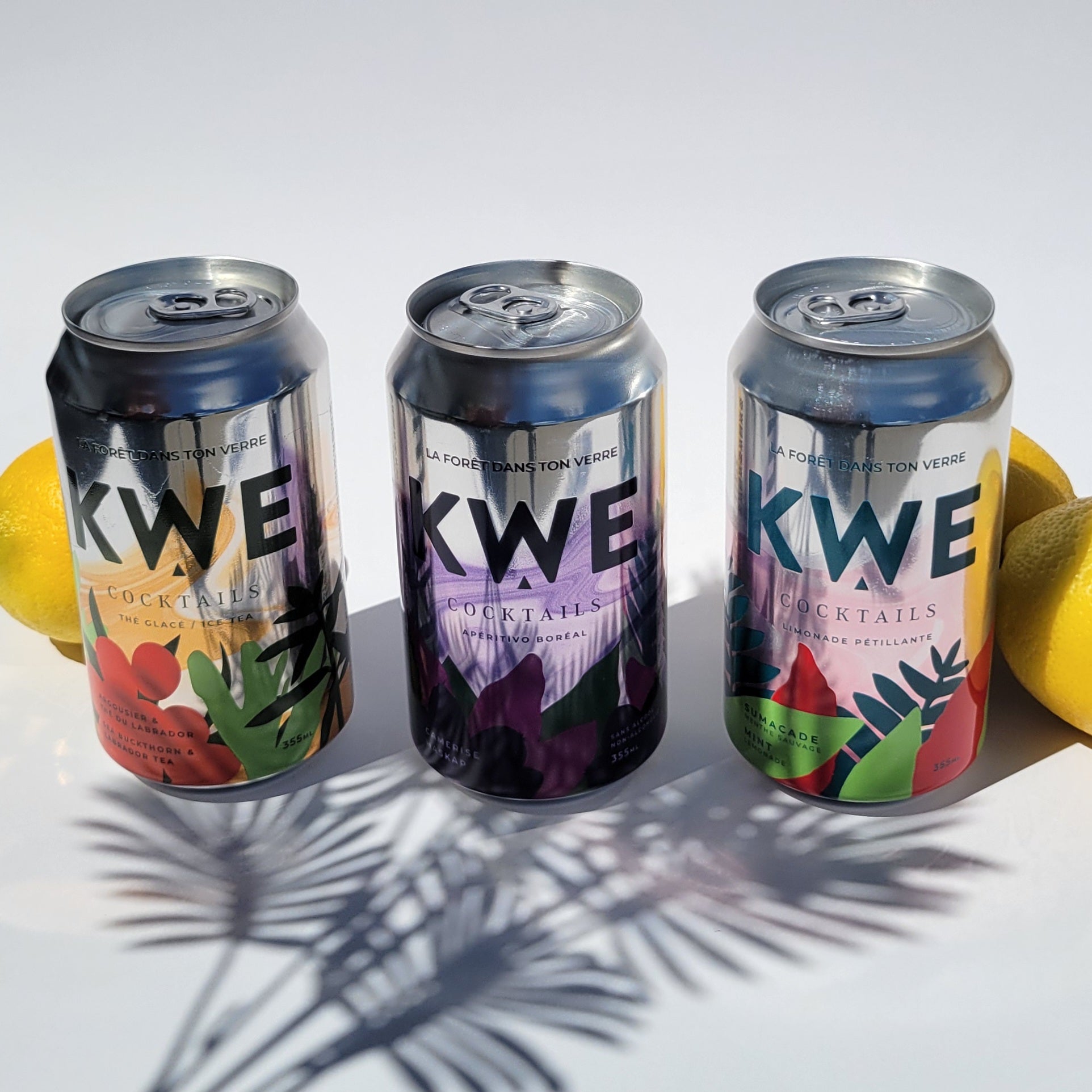 Three KWE cocktails cans with colorful designs on a white background