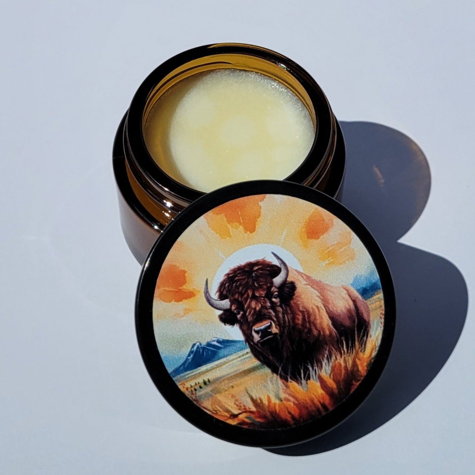 Cosmetic jar with a lid featuring a bison design on a light blue background